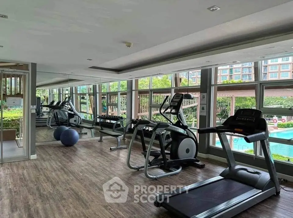 Modern gym with large windows and pool view in luxury residential complex.
