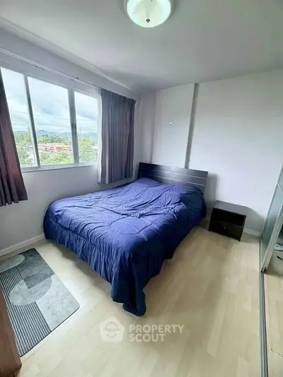Cozy bedroom with large window and wooden flooring, offering natural light and a serene atmosphere.