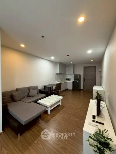Modern living room with open kitchen, cozy seating, and sleek wooden flooring.
