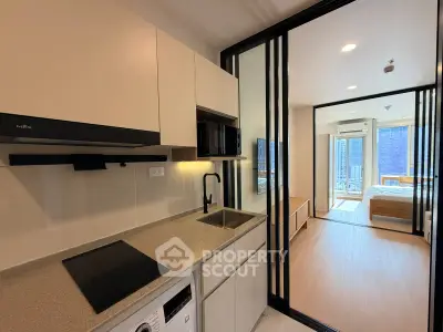 Modern apartment kitchen with sleek design and open layout leading to a bright bedroom.