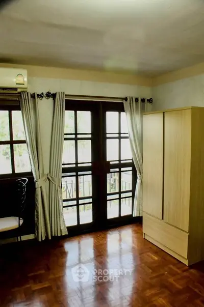 Bright bedroom with large window and wooden wardrobe, perfect for cozy living.