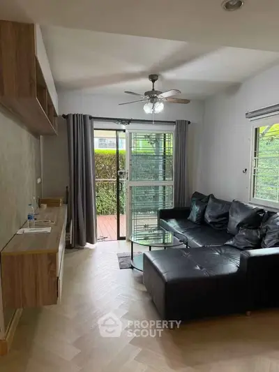 Modern living room with black leather sofa and glass coffee table, featuring natural light and garden view.