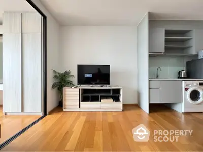 Modern living room with wooden flooring, TV unit, and compact kitchen area with washing machine.