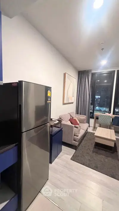 Modern living room with cozy seating and stainless steel fridge in a stylish apartment.