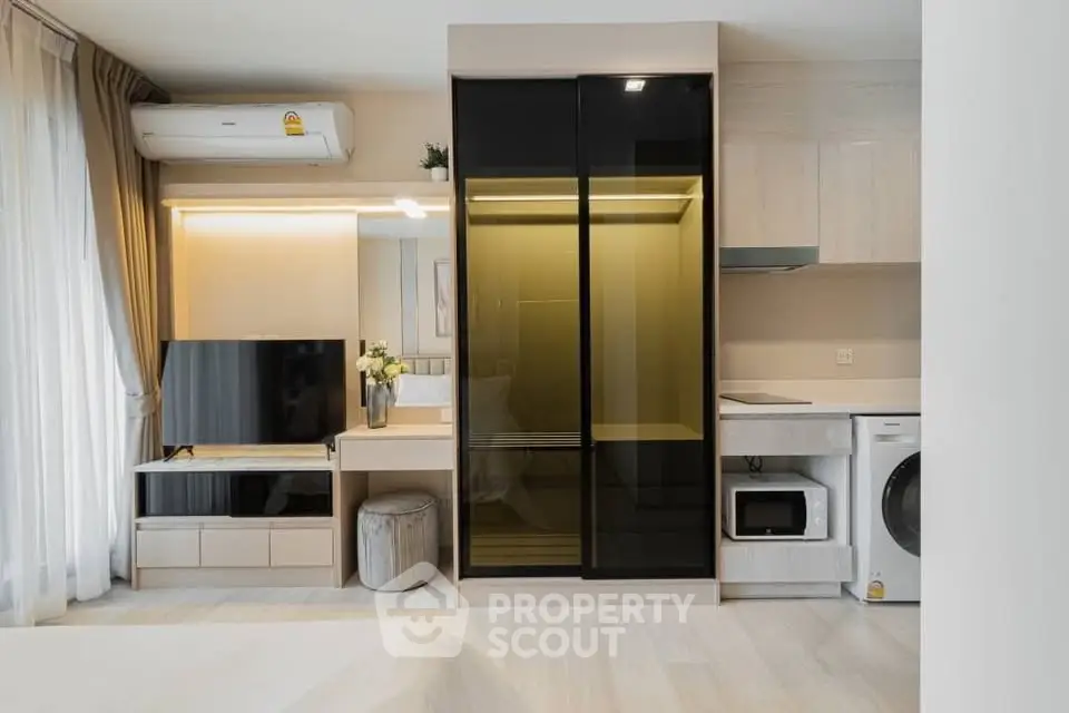 Modern studio apartment with sleek built-in storage, TV, and compact kitchen appliances.