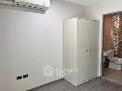 Minimalist bedroom with wardrobe and bathroom access, featuring air conditioning.