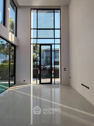 Spacious modern living room with high ceilings and large windows offering natural light and garden view.