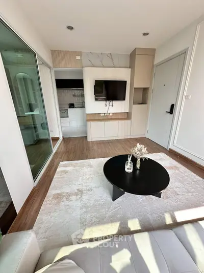 Modern living room with sleek design, featuring a wall-mounted TV, stylish coffee table, and open kitchen layout.