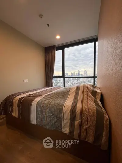 Cozy bedroom with city view and large window, featuring modern bedding and wooden flooring.