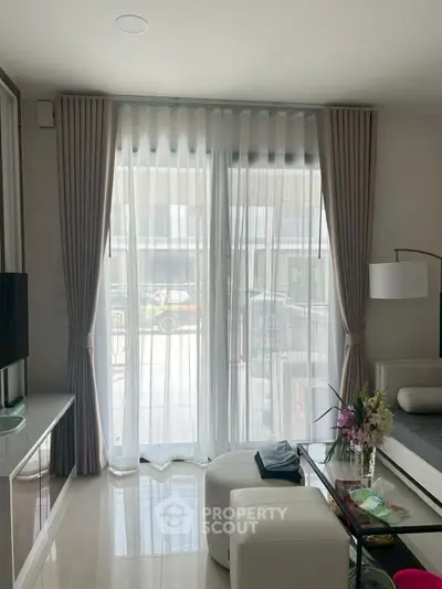 Modern living room with large windows and elegant decor, featuring sheer curtains and stylish furniture.