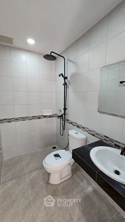 Modern bathroom with sleek fixtures and tiled walls, featuring a rainfall shower and contemporary sink.