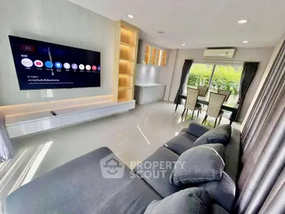 Modern living room with large TV and dining area overlooking greenery.