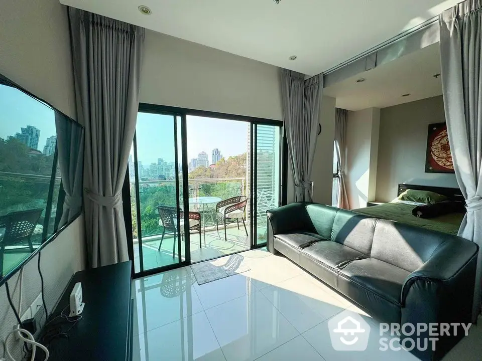 Modern living room with balcony and city view, featuring sleek furniture and abundant natural light.