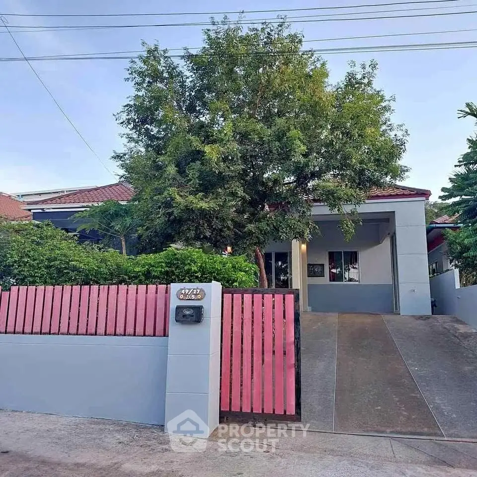 Charming single-story home with a red roof, lush greenery, and a welcoming driveway in a serene neighborhood.