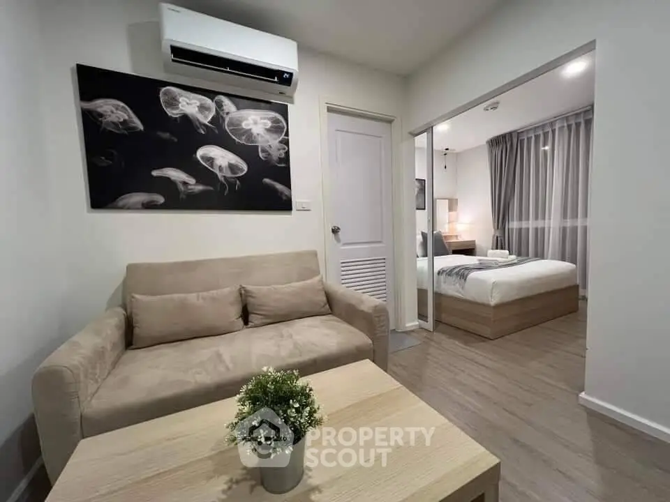 Modern living room with beige sofa, air conditioning, and view into cozy bedroom.