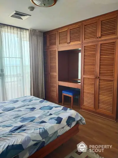 Spacious bedroom with large bed, wooden floor, built-in wardrobe, and ample natural light filtering through sheer curtains.