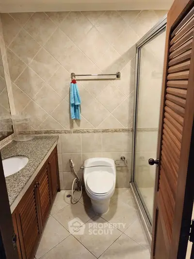 Compact bathroom with tiled walls, glass shower, and wooden cabinets.