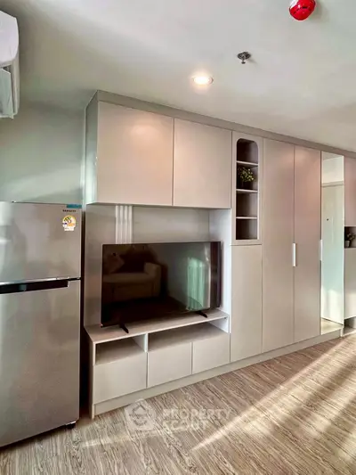 Modern living room with sleek built-in storage and TV unit, featuring a stainless steel fridge and stylish lighting.