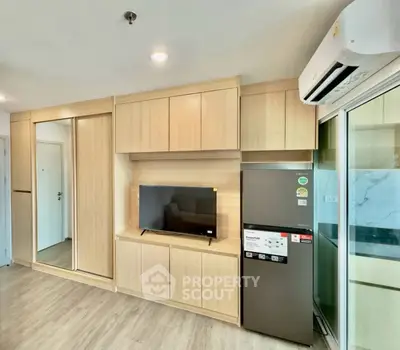 Modern living room with built-in wooden cabinets, TV, and sleek refrigerator in a cozy apartment.
