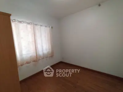 Spacious empty room with wooden flooring and window with curtains, perfect for customization.