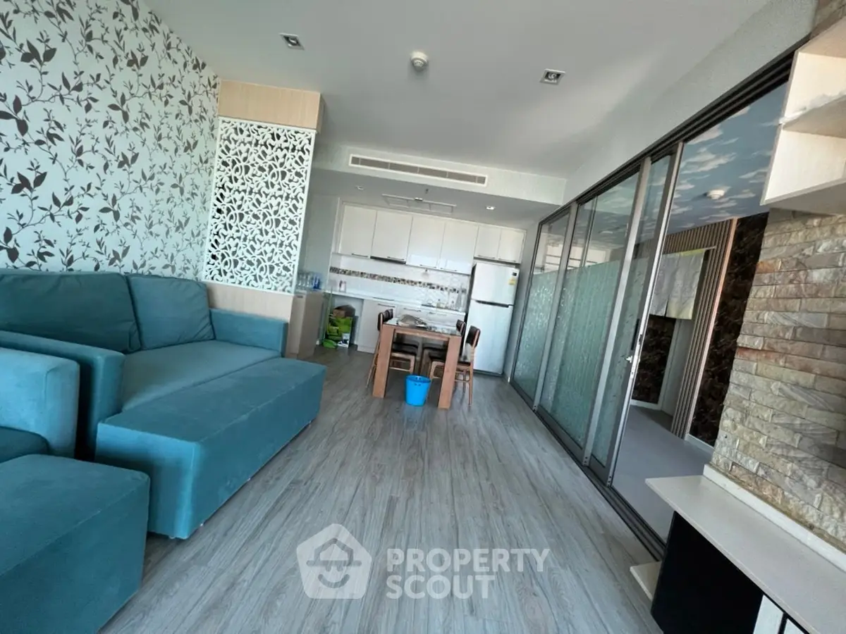 Modern living room with teal sofa and open kitchen layout, featuring stylish decor and ample natural light.