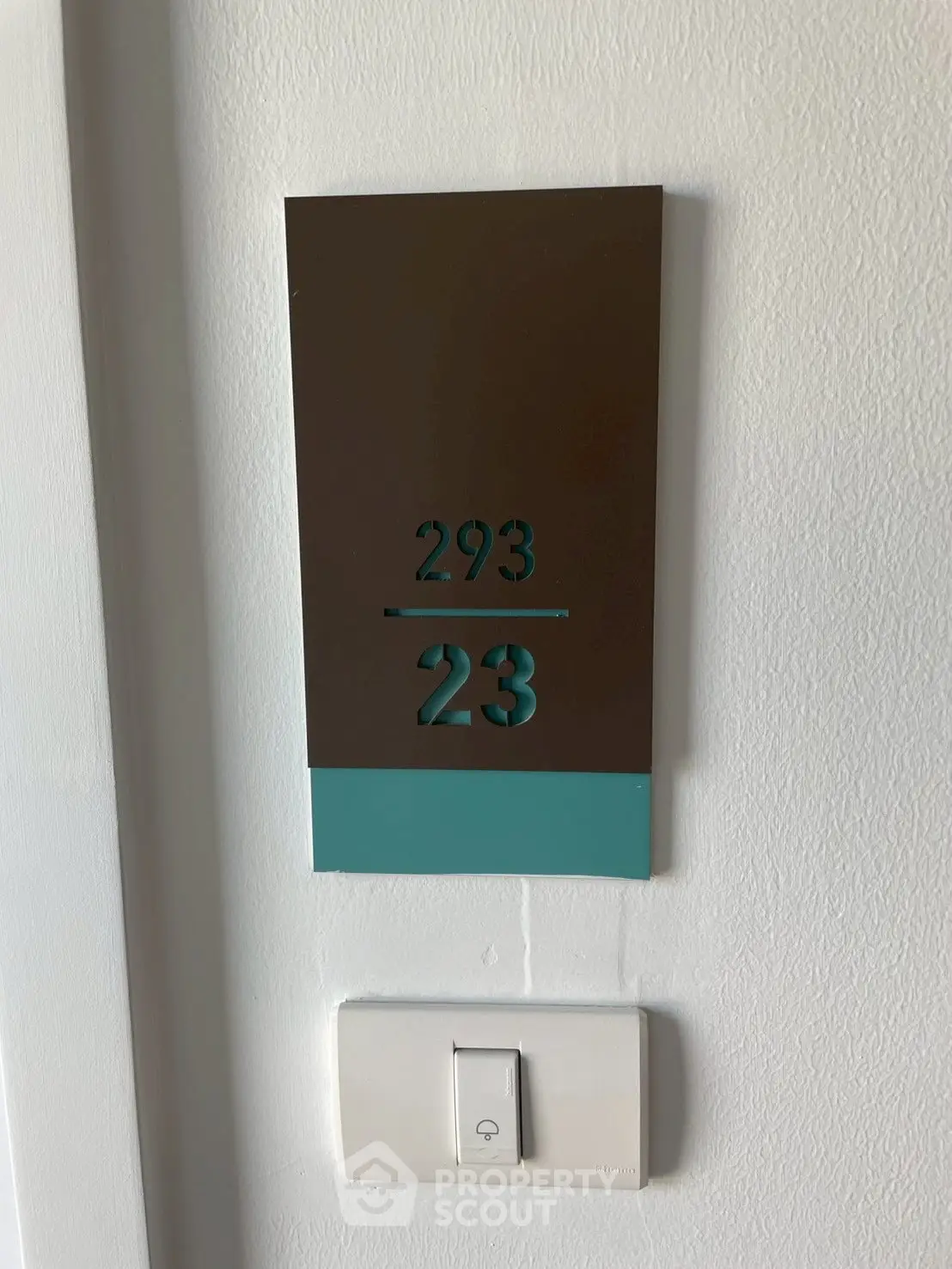 Modern apartment door number sign with sleek design and light switch below.