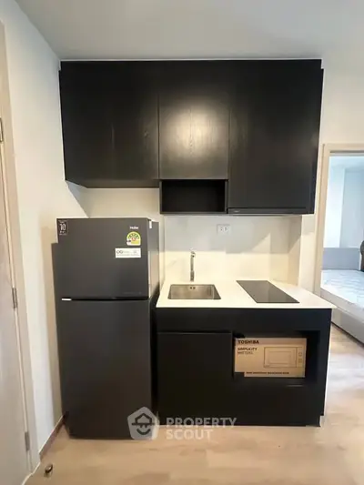 Modern compact kitchen with sleek black cabinets and appliances, featuring a fridge and built-in microwave.