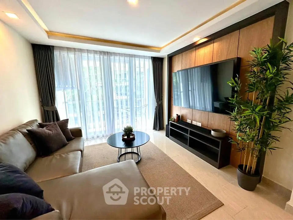 Modern living room with sleek furniture, large TV, and floor-to-ceiling windows offering natural light.