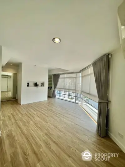 Spacious modern living room with large windows and wooden flooring in a high-rise apartment.