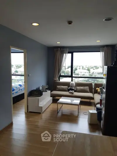 Modern living room with wooden flooring, cozy sofa, and large window offering natural light and scenic views.