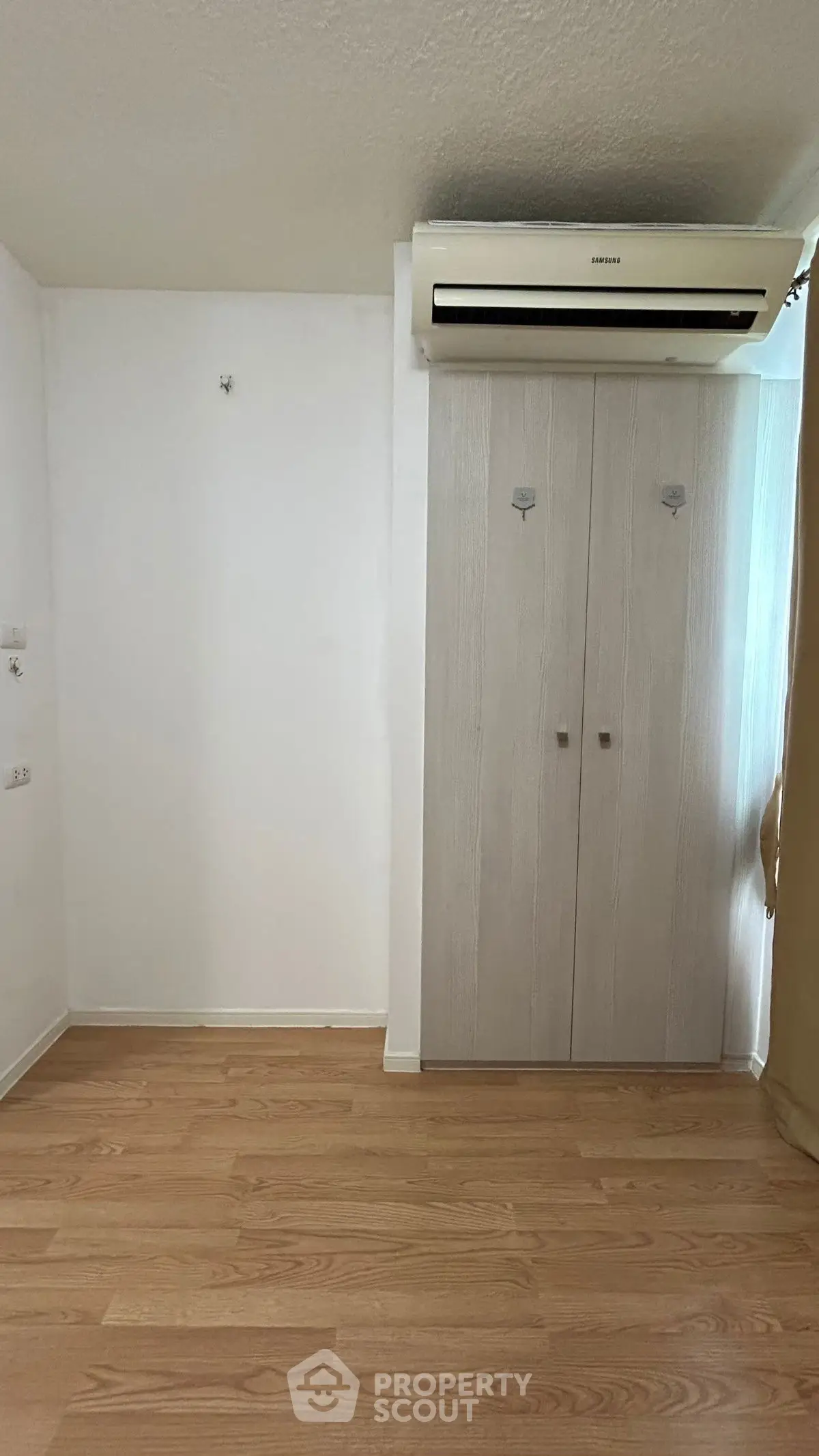 Spacious room with wooden flooring and built-in air conditioning unit.