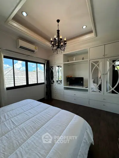Elegant bedroom with chandelier and built-in storage, featuring large windows and stylish decor.