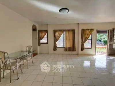 Spacious living room with large windows and tiled flooring, perfect for natural light and comfort.