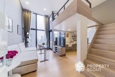 Modern duplex apartment with high ceilings, expansive windows, and a sleek staircase leading to an upper level, showcasing a spacious living area and a glimpse of the kitchen.