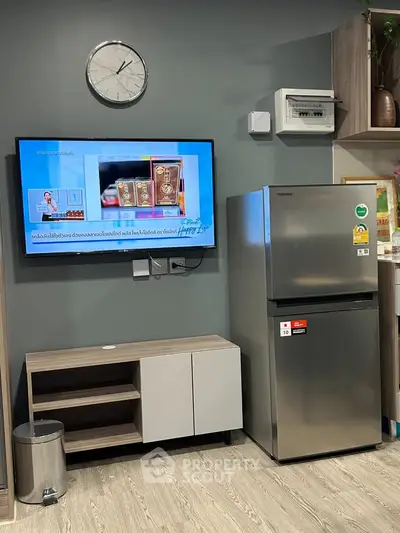 Modern kitchen with stainless steel fridge and wall-mounted TV, stylish cabinetry, and sleek flooring.