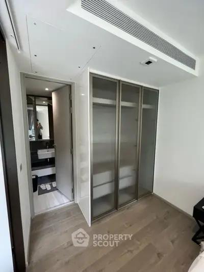 Modern apartment with sleek closet and bathroom view, featuring elegant wooden flooring and contemporary design.