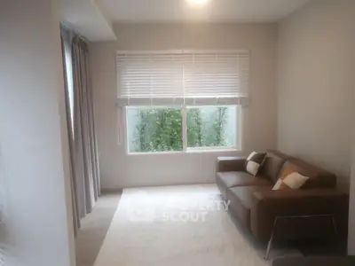 Bright living room with modern sofa and large window overlooking greenery.