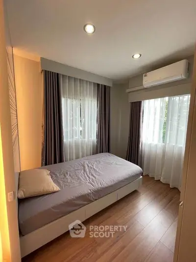 Cozy bedroom with modern decor and natural light, featuring hardwood floors and air conditioning.