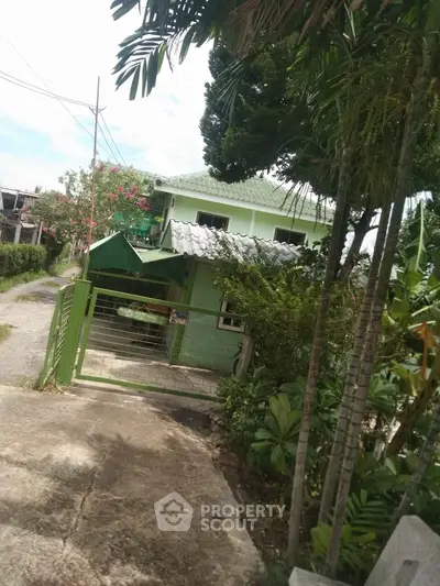 Charming two-story green house with lush garden and gated entrance in a serene neighborhood.