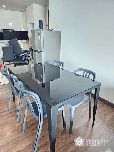 Modern dining area with sleek black table and chairs, adjacent to a contemporary kitchen.