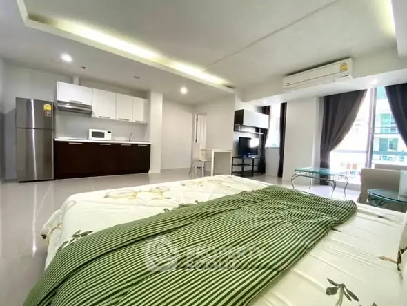 Spacious modern studio apartment with open kitchen and cozy living area, featuring large windows and contemporary furnishings.