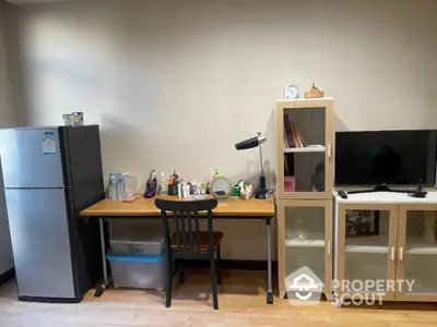 Cozy study area with desk, chair, fridge, and storage cabinets in modern apartment.