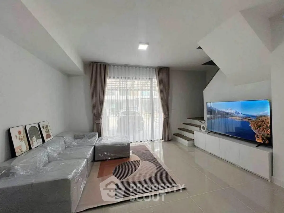 Modern living room with sleek design, large TV, and natural light from floor-to-ceiling window.