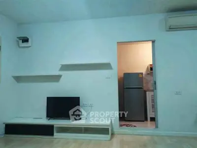 Modern living room with minimalist decor and adjacent kitchen area featuring a refrigerator.