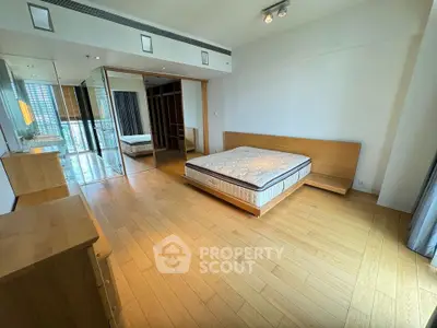 Spacious modern bedroom with wooden flooring and large mirrored closet in luxury apartment.
