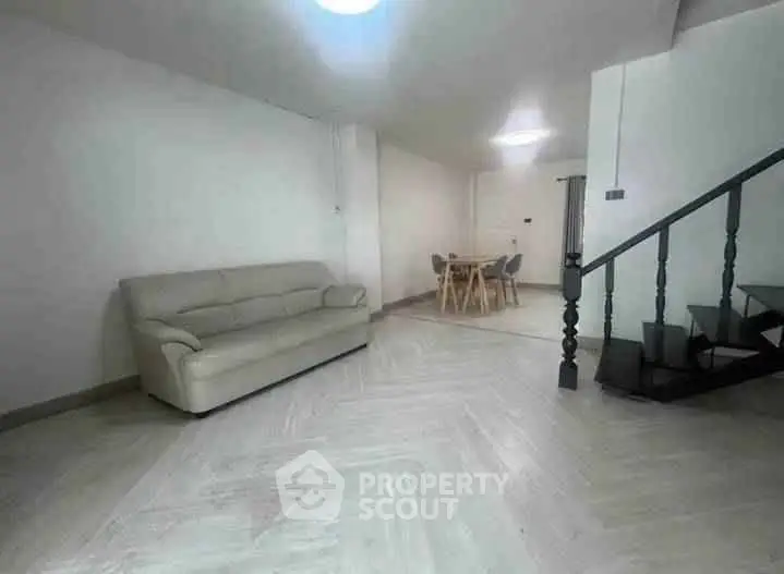 Spacious living room with modern sofa and dining area, featuring elegant staircase.
