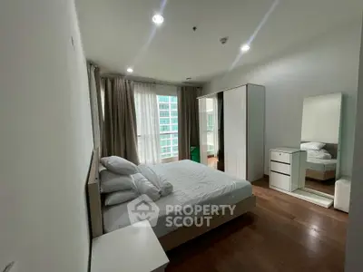 Spacious modern bedroom with large window and wooden flooring in high-rise apartment.