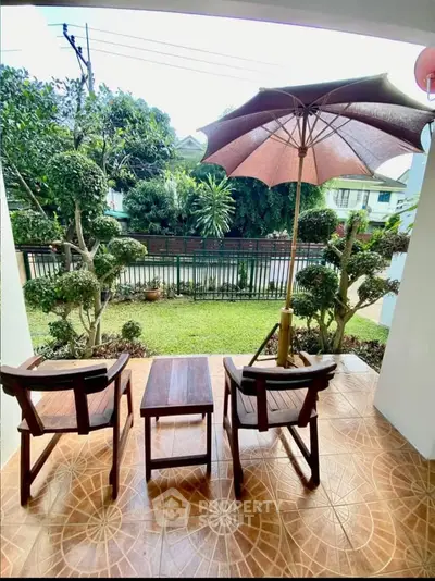 Charming garden view from a cozy balcony with seating and umbrella, perfect for relaxation.