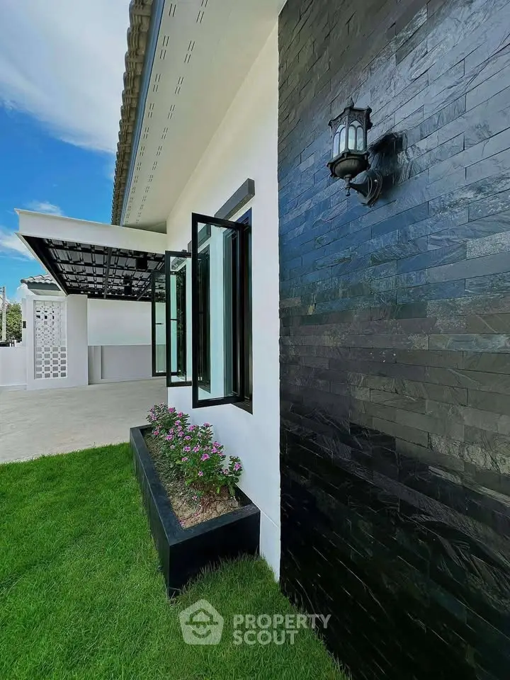 Modern house exterior with black stone wall, lush green lawn, and stylish outdoor lighting.