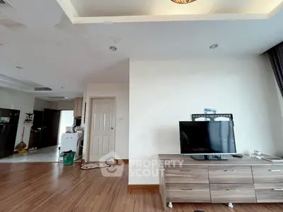 Spacious living room with modern decor and wooden flooring, featuring a TV unit and open kitchen layout.